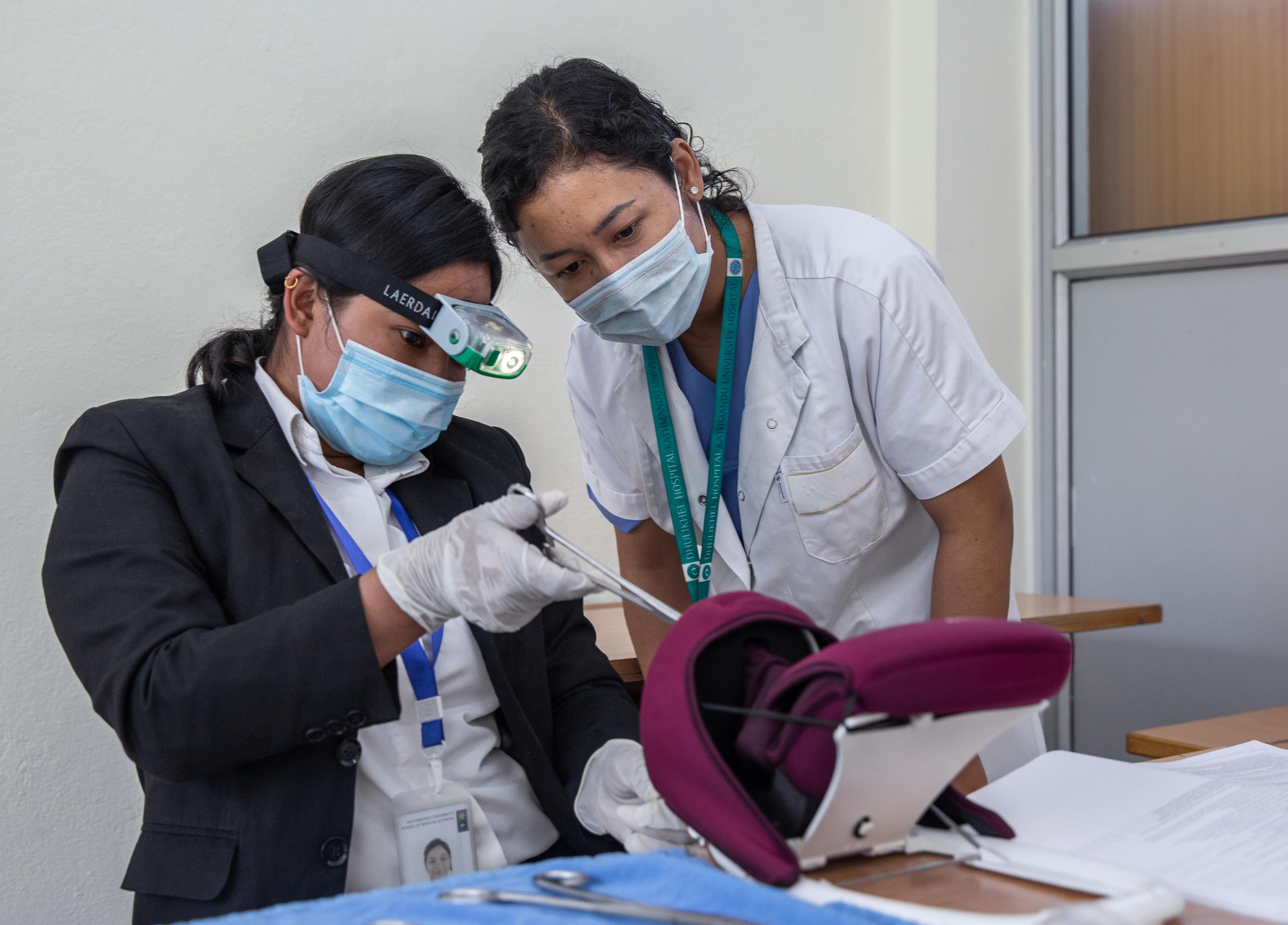 A midwifery student practices inserting an intrauterine device on a postpartum uterus trainer with the guidance of her teacher (right) at Kathmandu University School of Medical Sciences in Nepal.