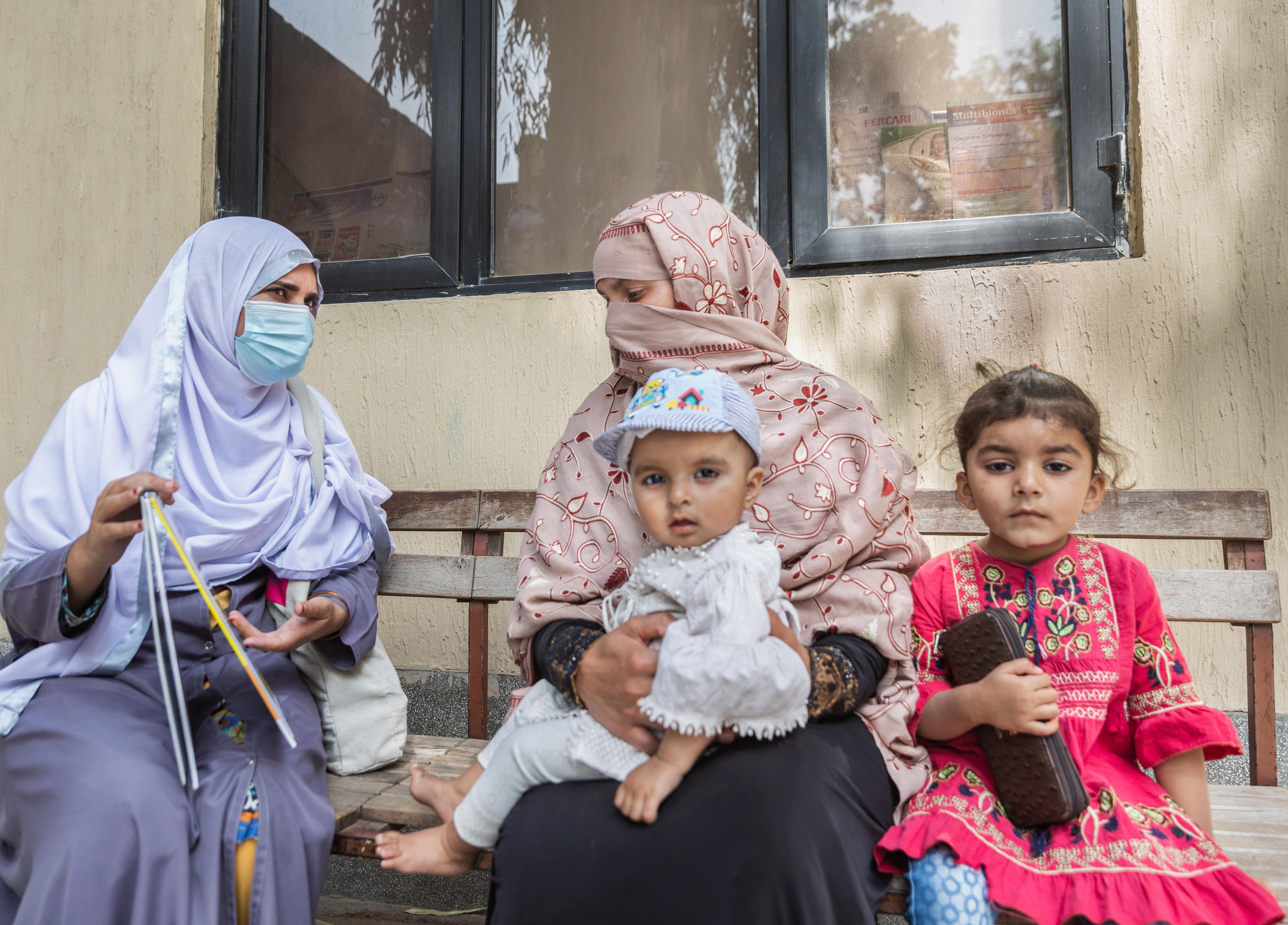 A health worker consults with a mother on various forms of contraceptives while she waits to see the doctor,  along with her children, aged 4 years and 9 months.