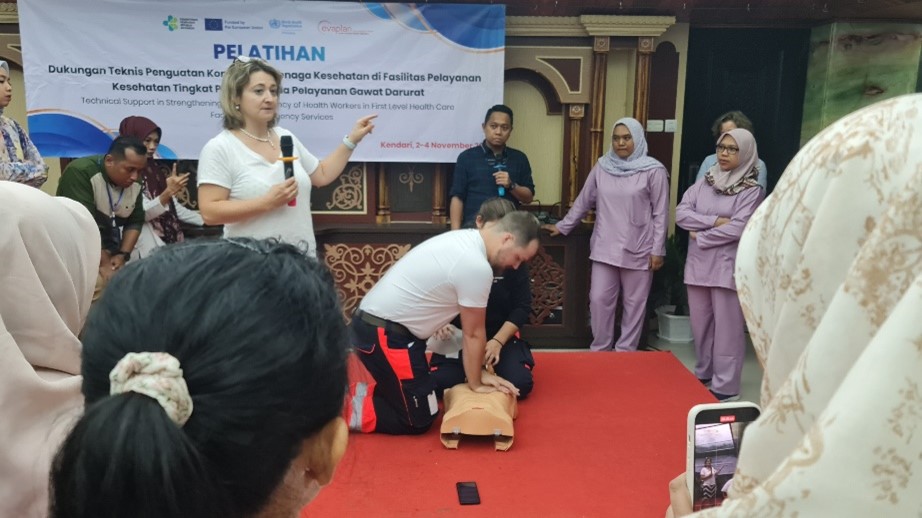 Healthcare workers during a training, paying attention to the instructors showing how to do CPR in the centre of the room.