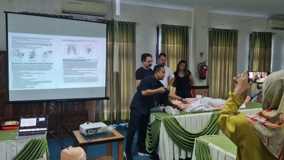 Instructors in front of a class, explaining about emergency response while pointing at a human adult doll.