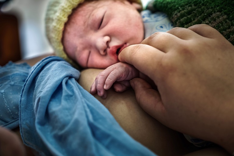 Newborn A newborn baby lays on her mother. The mother holds the baby's hand.